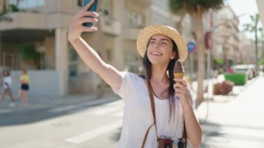 Genç İspanyol kadın turist akıllı telefonun yanında selfie çekiyor ve sokakta dondurma yiyor.