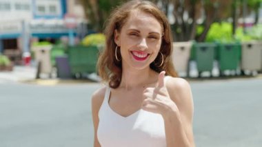 Young beautiful hispanic woman smiling confident doing ok sign with thumbs up at street
