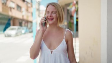 Young blonde woman talking on the smartphone walking at street