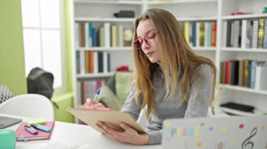 Kütüphane üniversitesinde belgeye yazı yazan beyaz kadın öğrenci