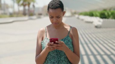 Afro-Amerikalı kadın parkta akıllı telefon kullanarak gülümsüyor.