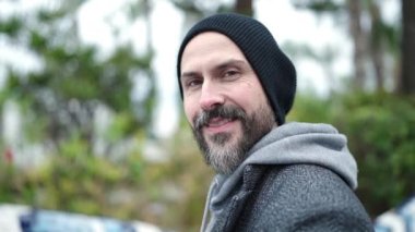 Genç kel adam parkta kendine güvenerek gülümsüyor.