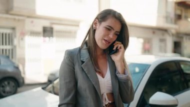 Genç bir kadın akıllı telefondan konuşuyor. Sokakta arabaya yaslanıyor.