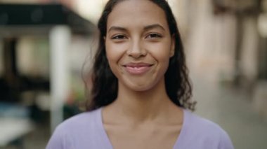 Afro-Amerikalı genç bir kadın kahvecinin terasında kendine güvenerek gülümsüyor.
