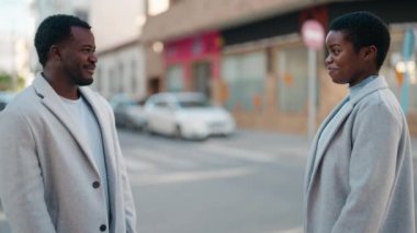 Afroamerikan çift sokakta el ele tutuşup gülümsüyor.