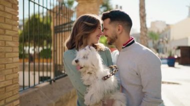 Young couple smiling confident holding dog at street