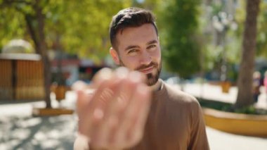 Genç İspanyol adam gülümsüyor. Kendine güveniyor. Parkta el kol hareketi yapıyor.