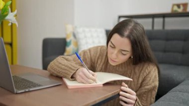 Genç ve güzel İspanyol kadın dizüstü bilgisayar kullanıyor. Evdeki deftere yazıyor.