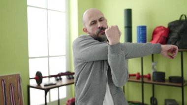 Spor merkezinde omuz ağrısı çeken kel genç bir adam.