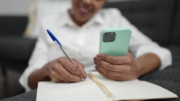 African American Woman Using Smartphone Writing Notebook Home — Vídeos de Stock
