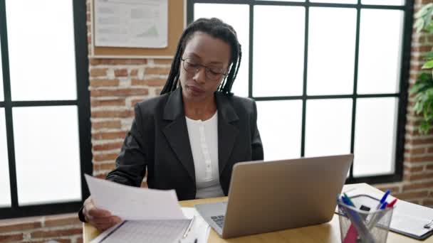 アフリカ系アメリカ人の女性ビジネスワーカーがオフィスでノートパソコン読み取り文書を使う — ストック動画
