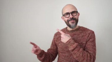 Genç kel adam gülümsüyor. Kendinden emin, izole edilmiş beyaz arka planda parmakları kenarı işaret ediyor.