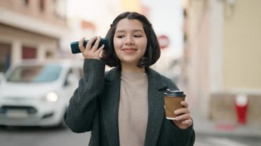 Genç İspanyol kız kahve içiyor. Caddedeki akıllı telefondan gelen sesli mesajları dinliyor.