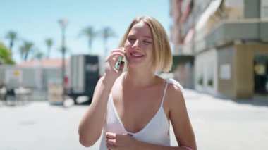 Young blonde woman talking on the smartphone walking at street