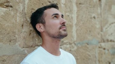 İspanyol asıllı genç adam izole edilmiş taş zeminde ciddi bir ifadeyle gökyüzüne bakıyor.