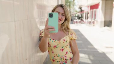 Genç ve güzel İspanyol kadın gülümsüyor. Kendine güveni tam. Sokakta akıllı telefonun yanında selfie çekiyor.