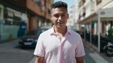 Sokakta yürürken kendinden emin gülümseyen genç Latin adam.