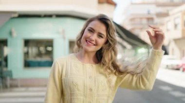 Young blonde woman smiling confident combing hair with hand at street