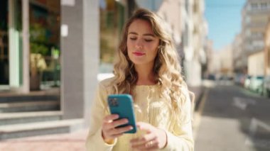 Young blonde woman smiling confident making selfie by the smartphone at street