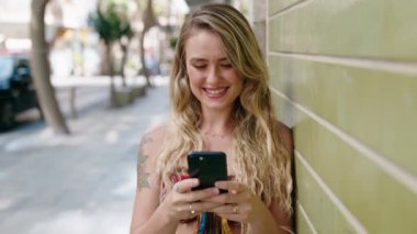 Sokakta akıllı telefon kullanan, kendine güvenen genç sarışın kadın.