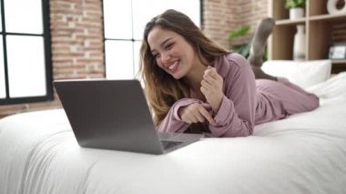 Young beautiful hispanic woman having video call lying on bed at bedroom