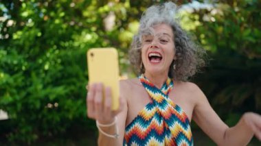Middle age grey-haired woman smiling confident having video call at park