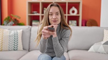 Kafkasyalı genç bir kadın evdeki kanepede televizyon izliyor.