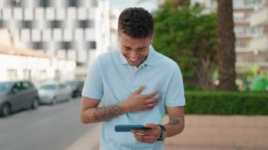 Afro-Amerikalı adam gülümsüyor. Parktaki akıllı telefondan videoyu izlediğinden emin.