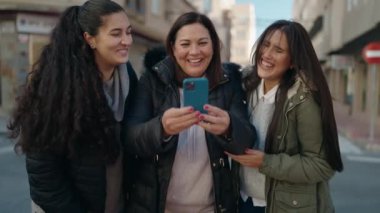 Mother and daughters smiling confident using smartphone at street