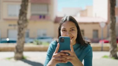 Genç Afro-Amerikalı kadın sokakta akıllı telefon kullanarak gülümsüyor.