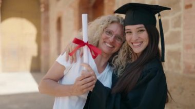 Two women mother and graduated daughter hugging each other at campus university