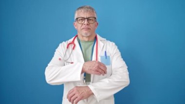 Orta yaşlı, gri saçlı, gülümseyen, kendine güvenen bir doktor. Kollarını çapraz yapıp, mavi arka planda duruyor.