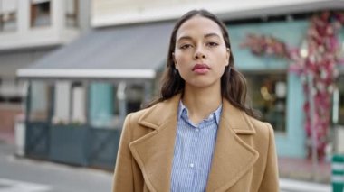 Ciddi bir ifadeyle duran ve kahve dükkanının terasında kollarını kavuşturan genç, güzel İspanyol bir kadın.