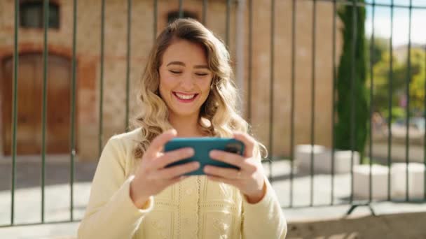 Mujer Rubia Joven Sonriendo Confiado Viendo Vídeo Teléfono Inteligente Calle — Vídeos de Stock