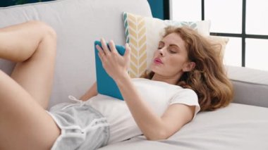 Evdeki kanepede uzanmış dokunmatik ped kullanan genç, güzel İspanyol kadın.