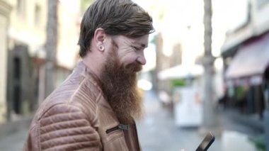 Young redhead man smiling confident using smartphone at street
