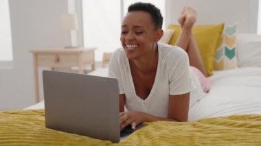 African american woman using laptop lying on bed at bedroom