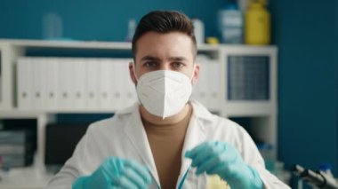 Laboratuvarda bilim adamı üniforması ve tıbbi maske giyen genç İspanyol adam.