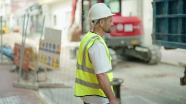 Orta yaşlı mimar gülümsüyor. Kollarını kavuşturup caddede duruyor.