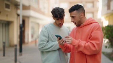 Genç İspanyol çift sokakta akıllı telefon kullanıyor.