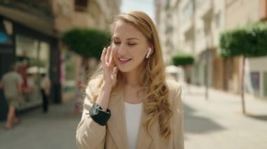 Genç sarışın kadın sokakta müzik dinliyor.