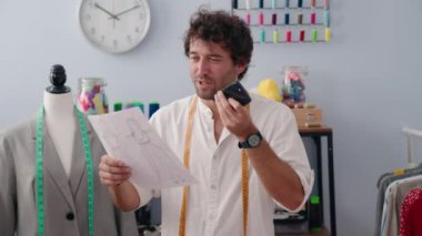 Genç İspanyol terzi akıllı telefondan konuşuyor giyim fabrikasında kıyafet tasarımı yapıyor.