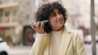 Young woman smiling confident listening audio message by the smartphone at street