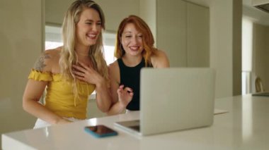 Two women having video call sitting on table at kitchen