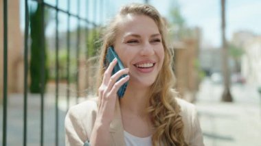 Genç sarışın kadın gülümsüyor. Kendine güveni tam. Akıllı telefondan konuşuyor.