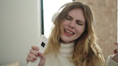 Young blonde woman listening to music and singing song at home