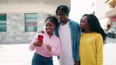 Afro-Amerikalı arkadaşlar yan yana durur, caddede akıllı telefonun yanında selfie çekerler.
