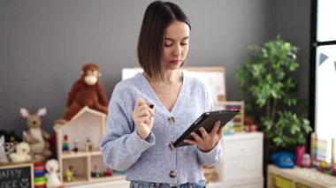 Young beautiful hispanic woman working as a teacher using touchpad at kindergarten