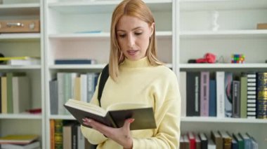 Young blonde woman student smiling confident reading book at university classroom
