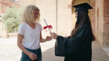 Two women mother and graduated daughter hugging each other at campus university